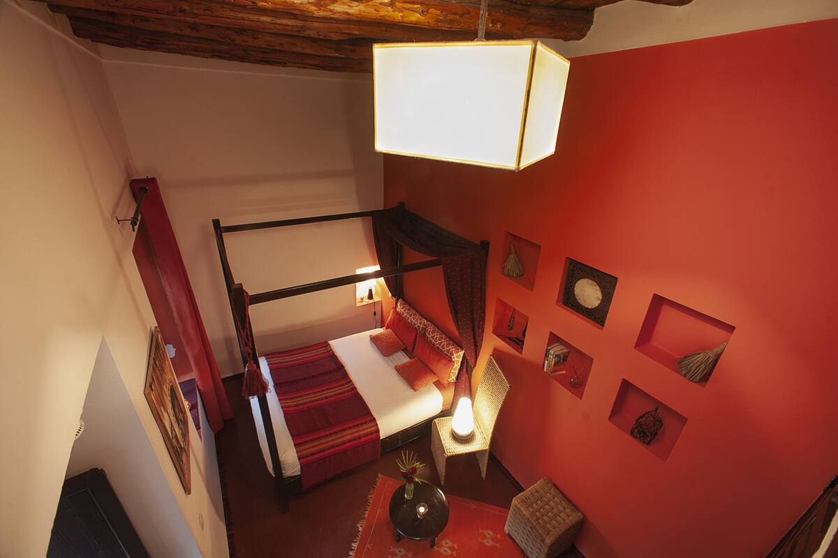A room with a four-poster bed, red walls, and a hanging light fixture.