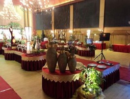 Un salón de banquetes con mesas redondas cubiertas con manteles rojos, decorado con jarrones y plantas.