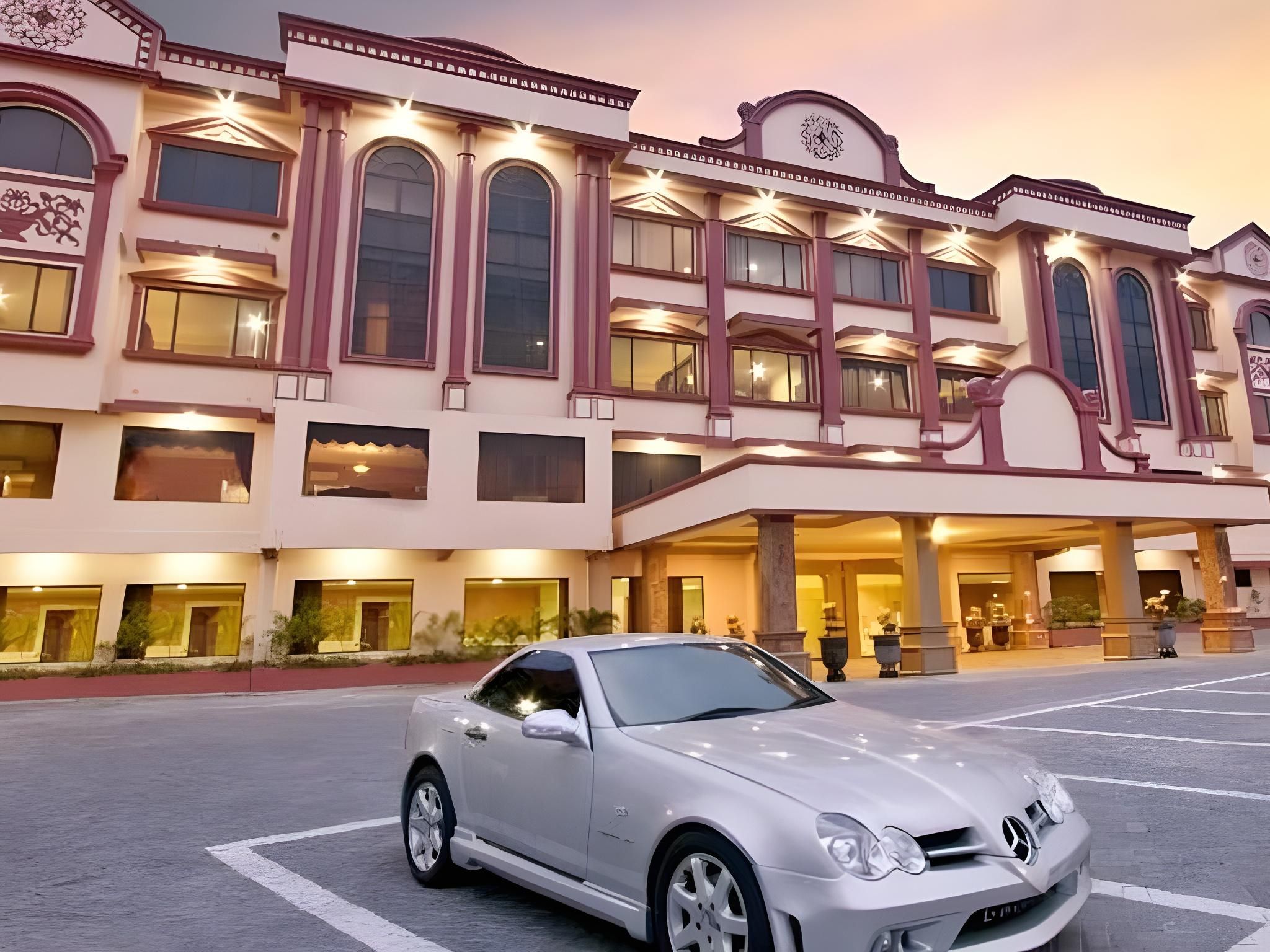 A white car parked in front of a hotel with a classic architectural style, featuring multiple windows and a grand entrance.