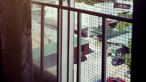 A view through a window with a metal grid, featuring a parking lot with several cars and a building in the background. - Remi hotel (Nha Trang)