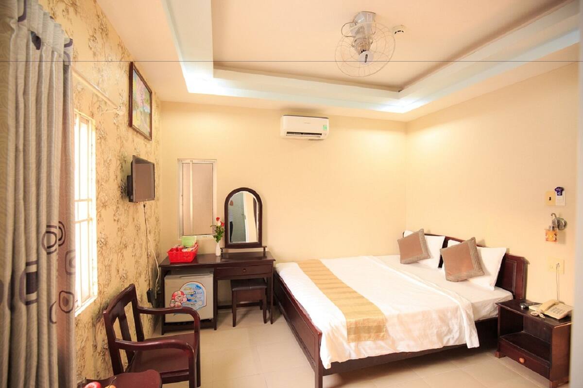 A bedroom with a bed, bedside table, desk, chair, and an air conditioning unit.