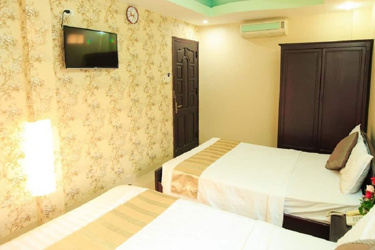 A hotel room with two beds, a television on the wall, a ceiling fan, and a wardrobe.