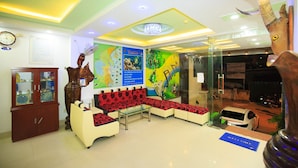 A lobby with a red and white sofa set, a wooden cabinet with glass doors, a map on the wall, and a chandelier. - Remi hotel (Nha Trang)