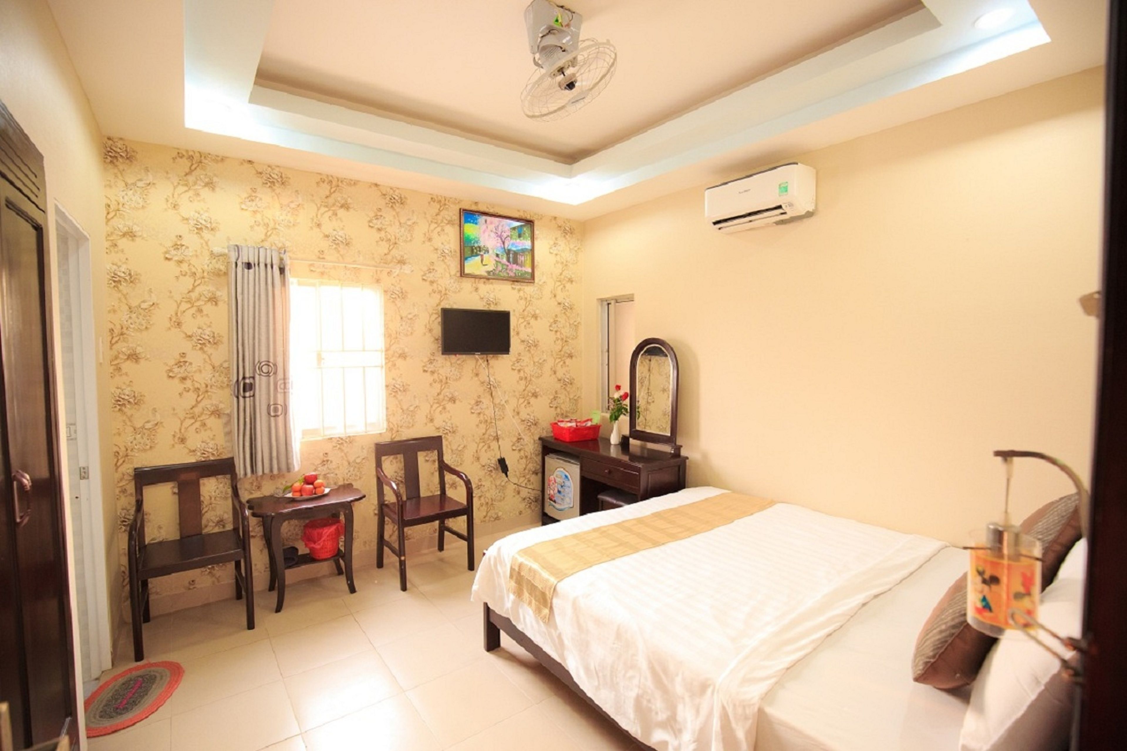 A hotel room with a bed, a desk, a chair, a TV, and an air conditioning unit.
