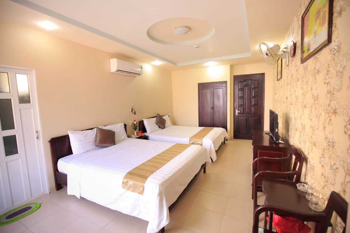 A hotel room with two beds, a desk with chairs, a television, and a door.
