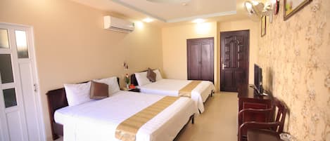 A hotel room with two beds, a desk with chairs, a television, and a door.