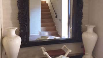 Un espejo con un marco ornamentado, una silla blanca y dos jarrones blancos.