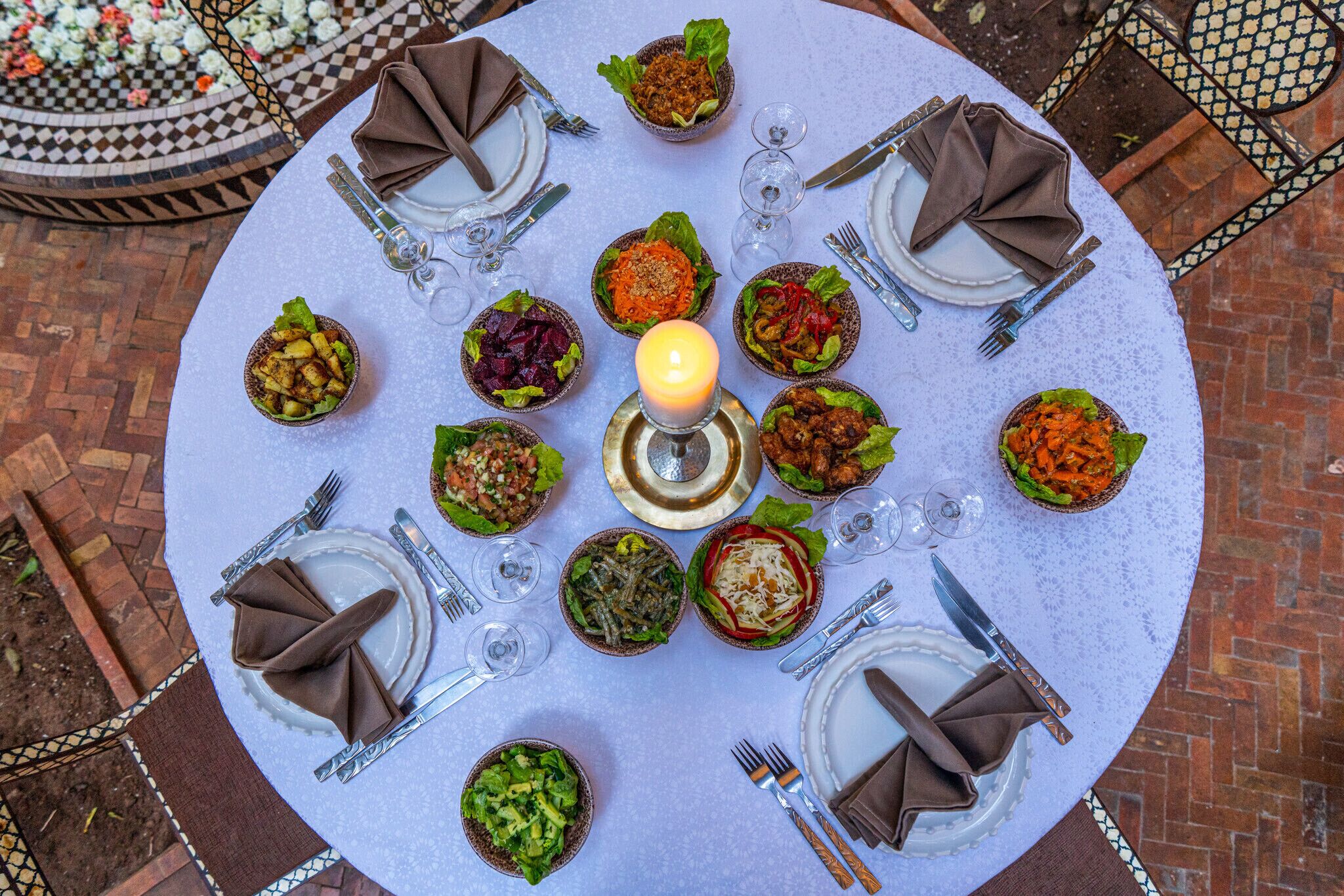 A round table with multiple dishes and glasses, surrounded by chairs and a candle.