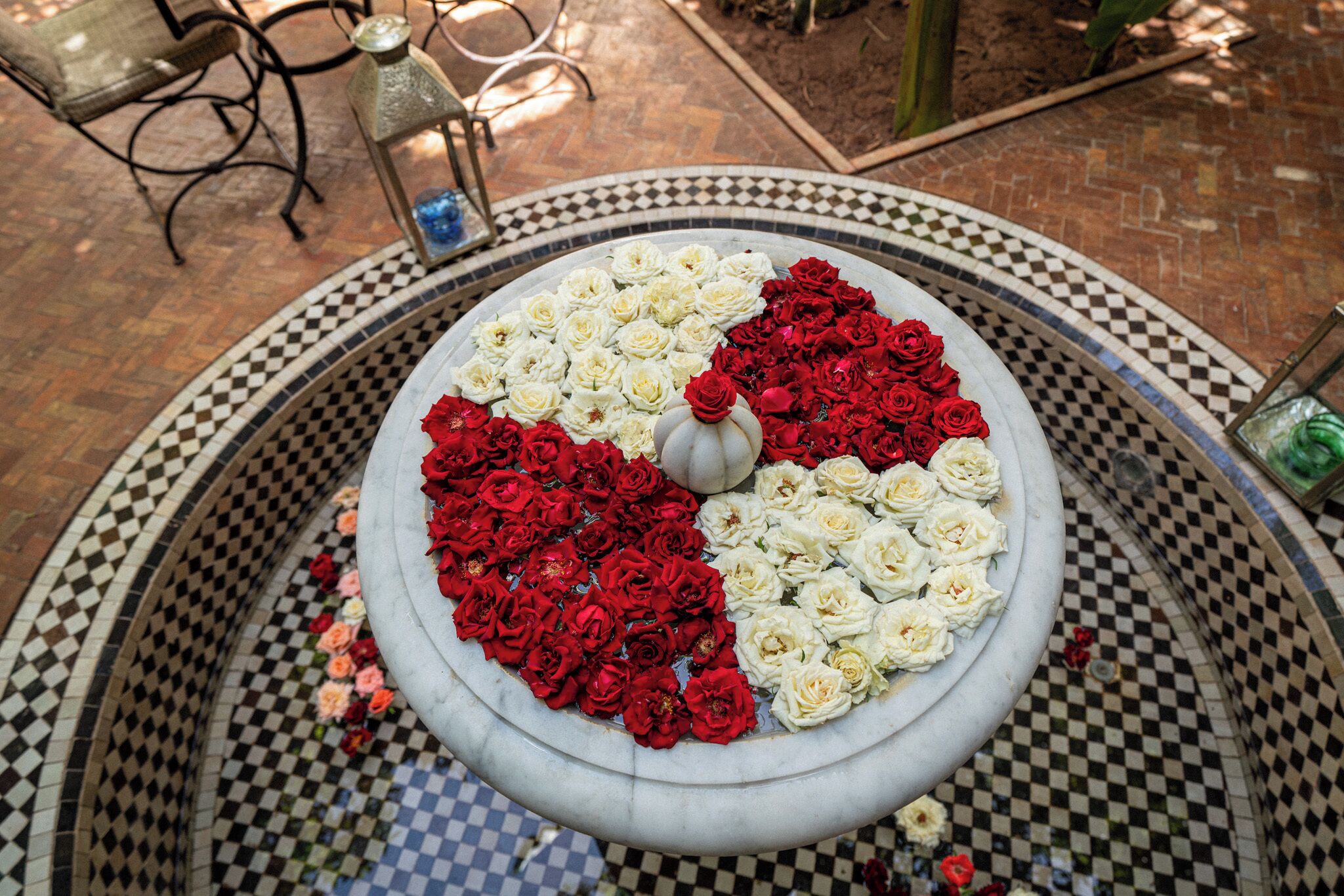A circular fountain with a checkered pattern around it, filled with red and white roses.