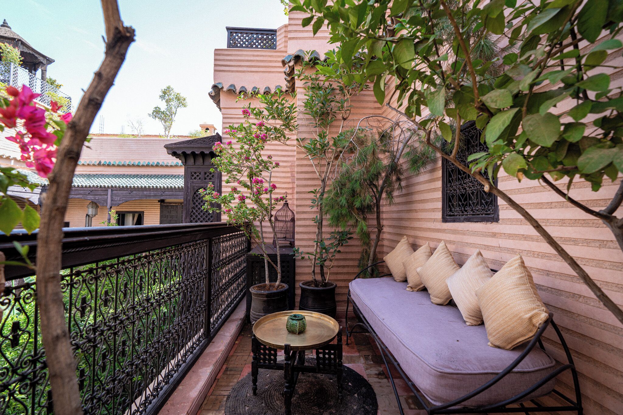 A balcony with a cushioned seating area, potted plants, and a decorative railing.