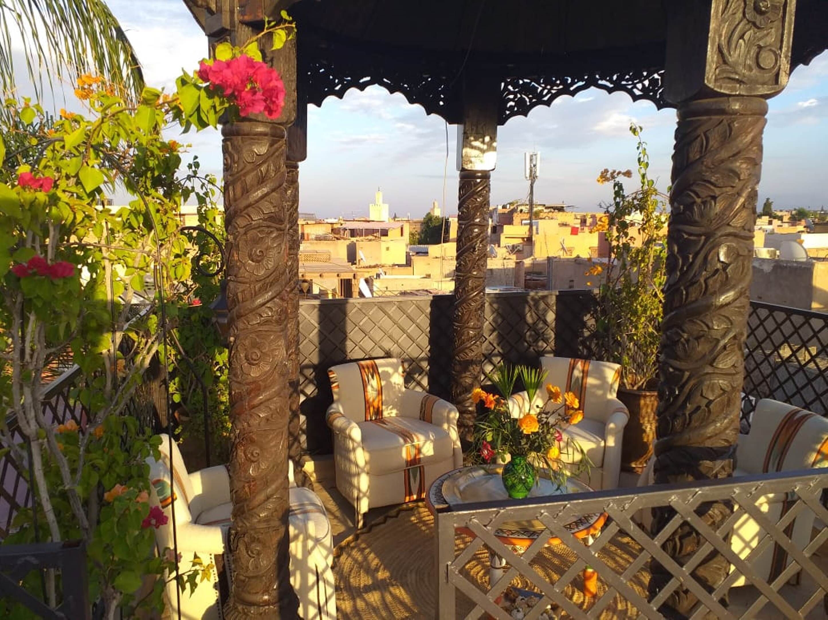 A rooftop terrace with ornate columns, white cushioned seating, and a view of the cityscape.