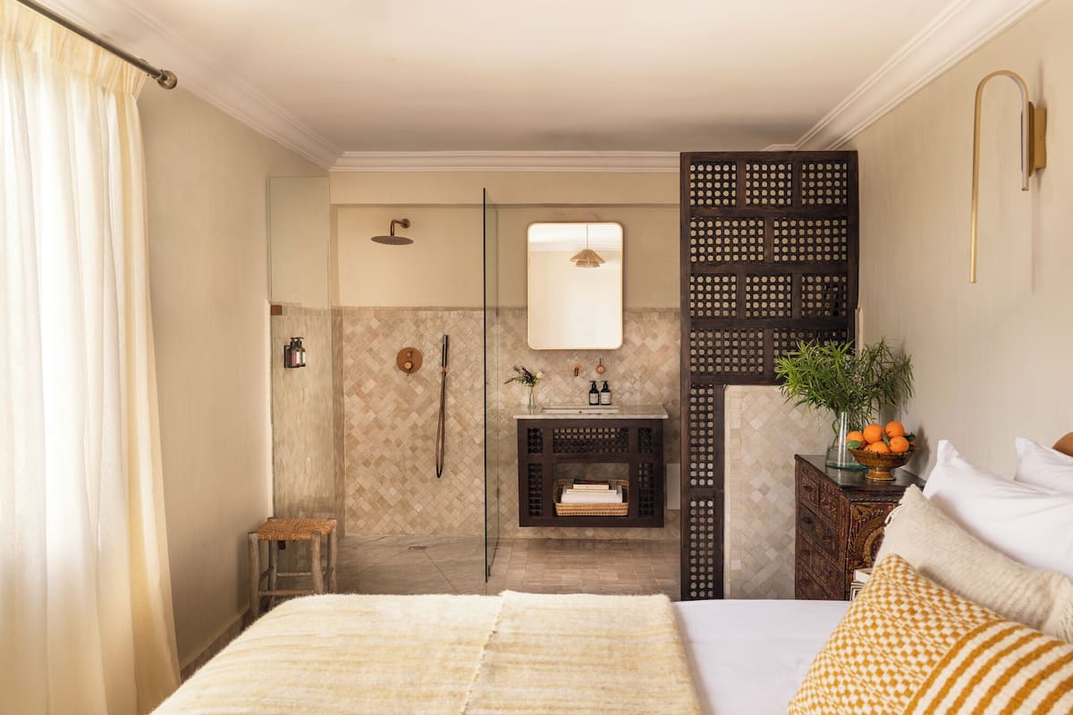A hotel room with a bed, a shower, a vanity with a mirror, and a decorative wall panel.