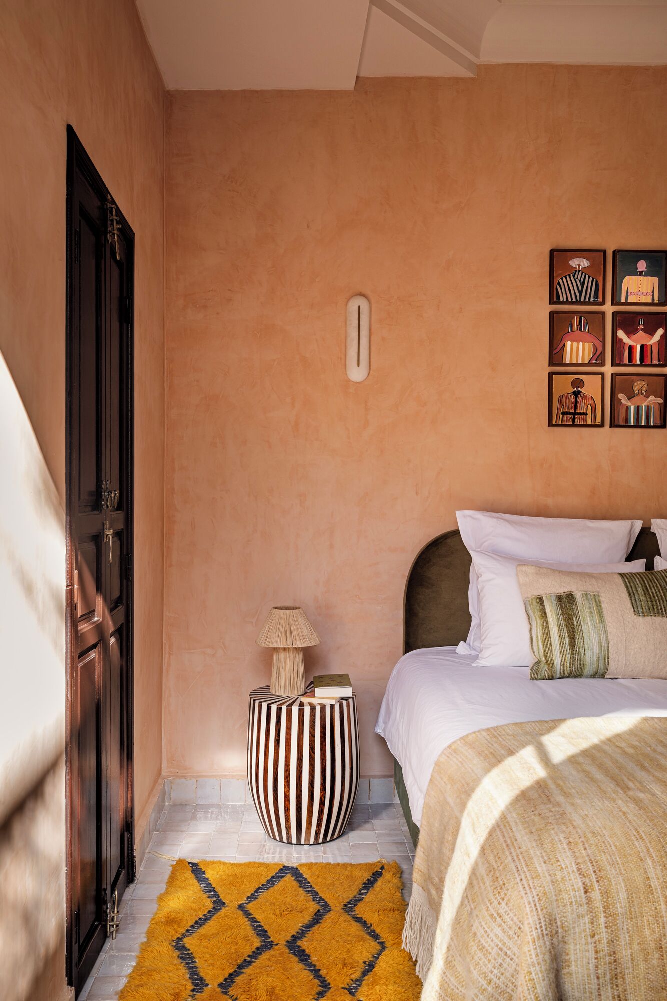 A bedroom with a bed, a nightstand, a lamp, a wall-mounted light, and a rug.