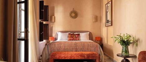 A hotel room with a bed, a chair, a round coffee table, a small side table, and a decorative wall piece.