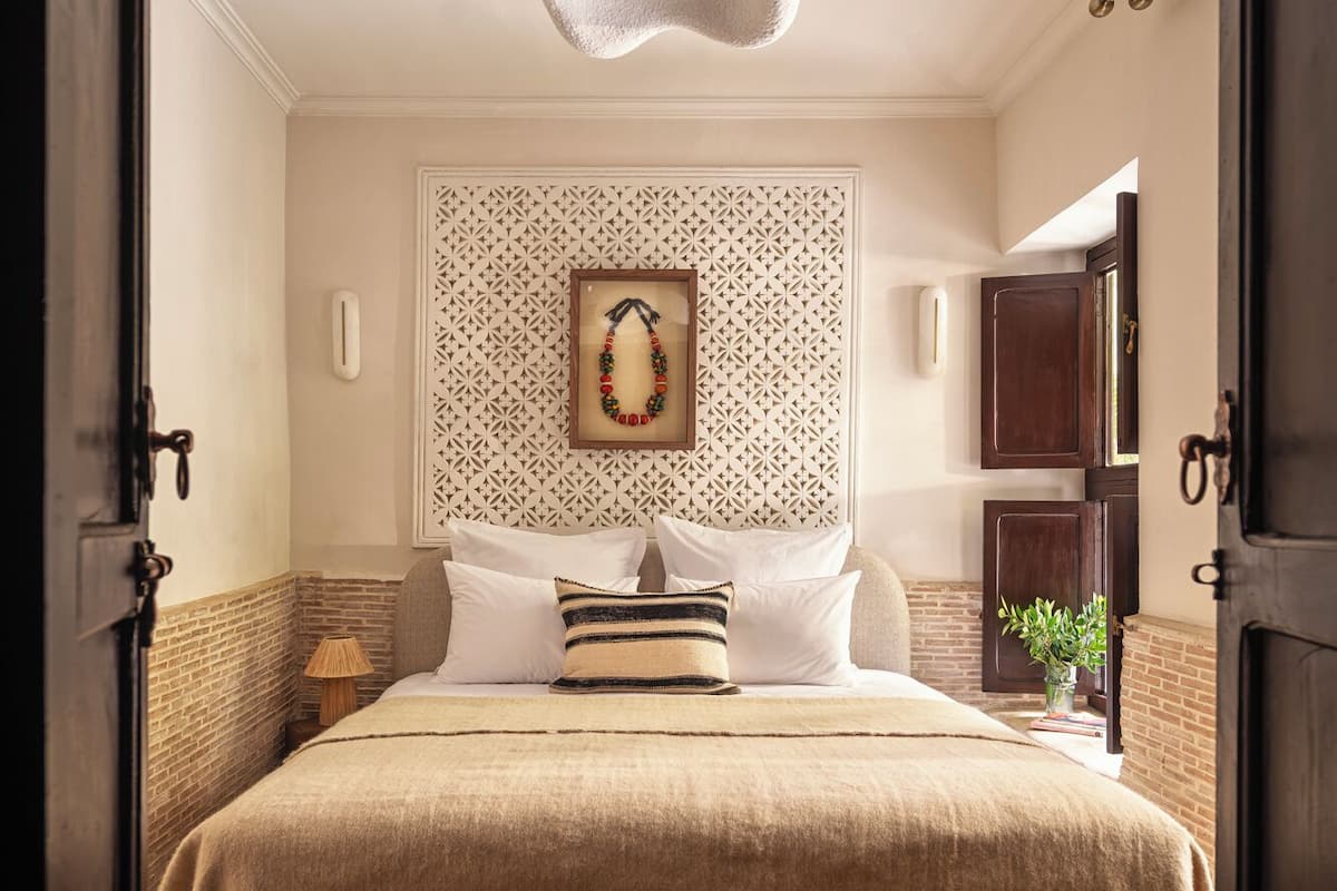 A bedroom with a bed, a wall-mounted light fixture, a patterned wall, and a small table with a plant.