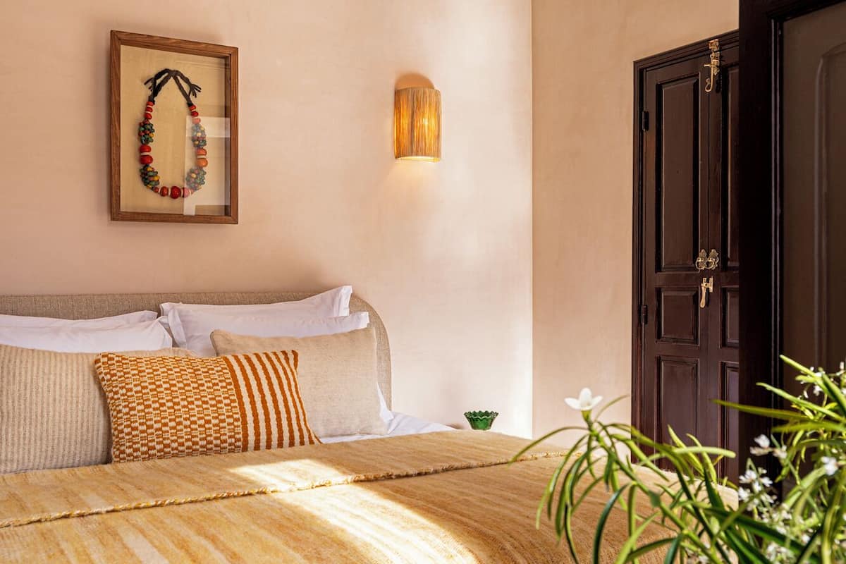 A bedroom with a bed, pillows, a wall-mounted light, a framed picture, and a door.