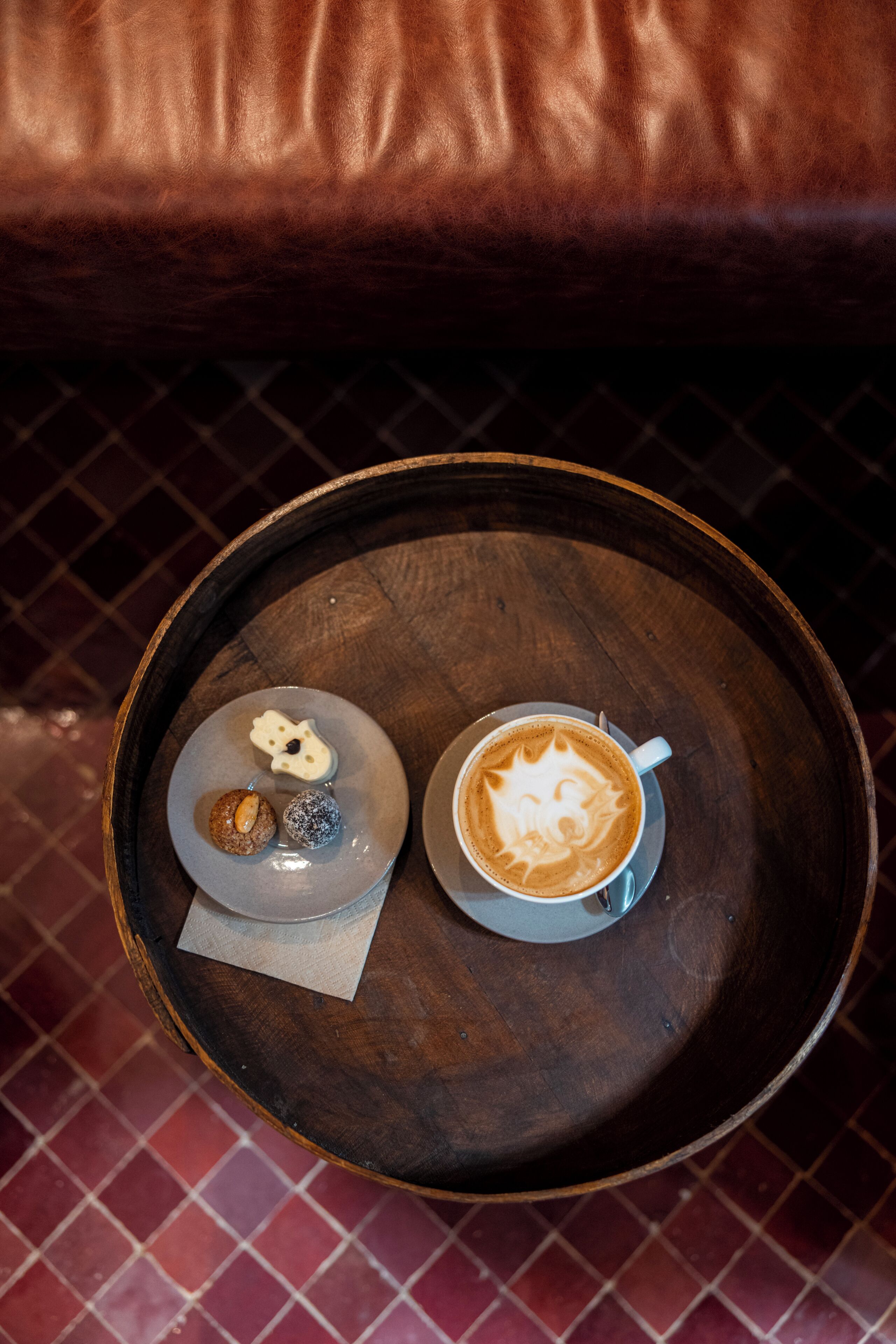 A round wooden tray with a cup of coffee and two pastries on a table.