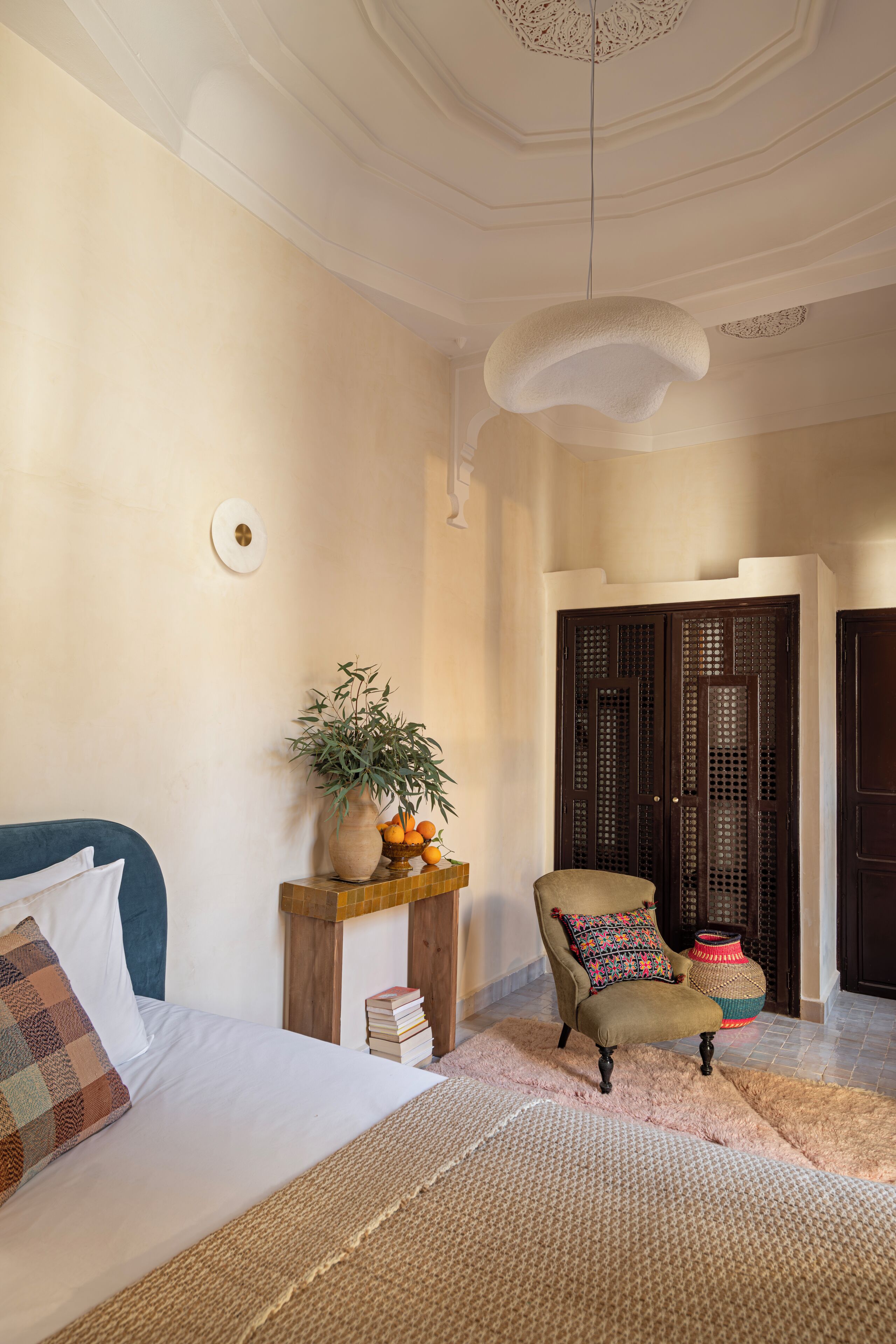 A bedroom with a bed, a chair, a small table with a plant, and a wardrobe.