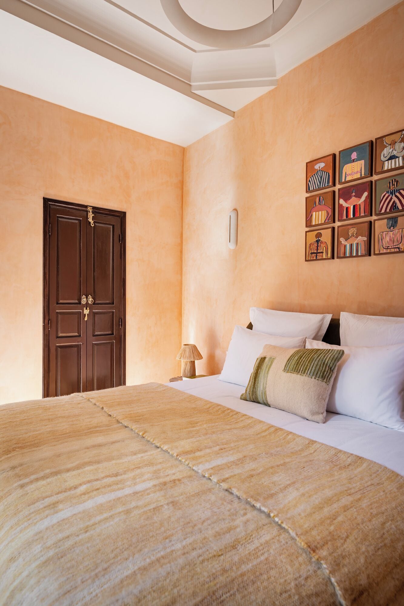 A bedroom with a large bed, a wooden door, and a wall with framed artwork.