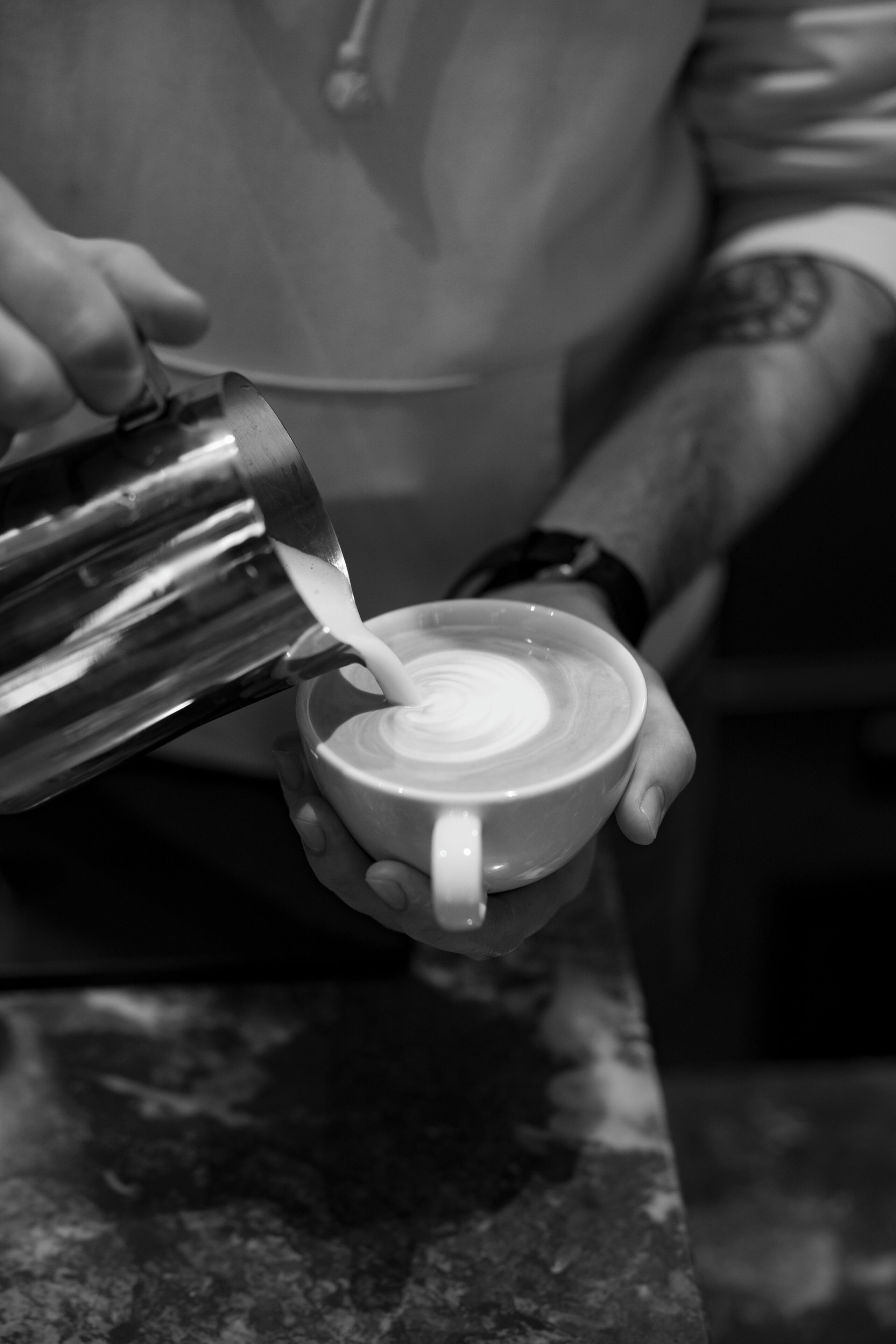 Jemand gießt Milch in eine Tasse, vermutlich in einem Café oder Coffeeshop.