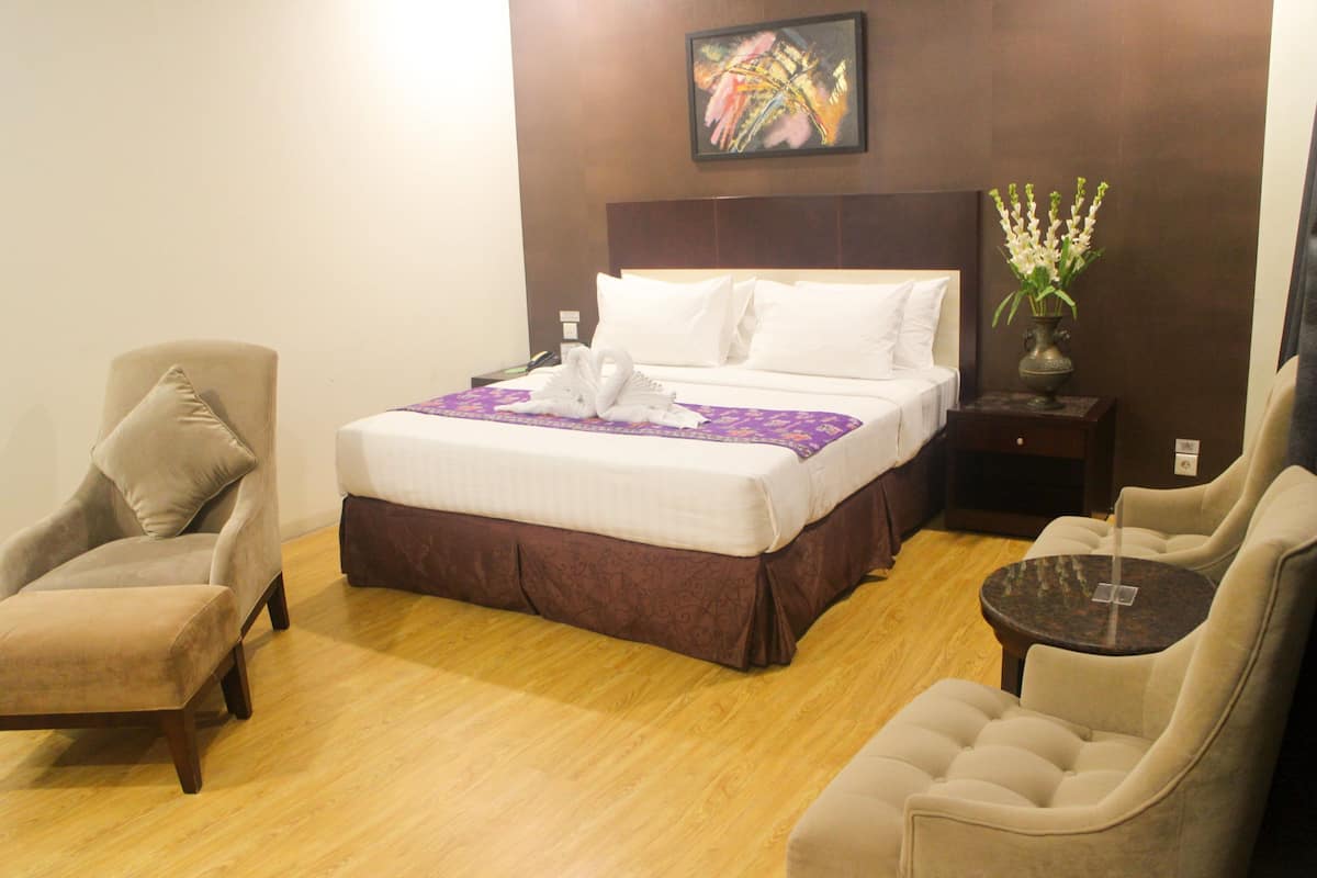 Une chambre d’hôtel comprenant un lit, deux fauteuils, une petite table, une table de chevet et un vase avec des fleurs.