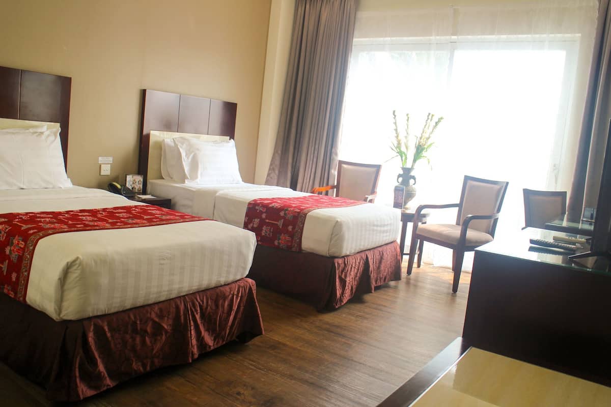 Une chambre d’hôtel avec deux lits, un bureau avec une chaise et une fenêtre avec des rideaux.