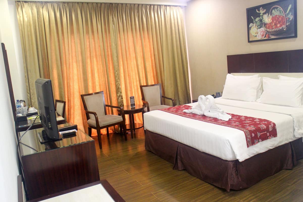 Une chambre d’hôtel comprenant un lit, un bureau avec un ordinateur, deux chaises et un téléviseur.