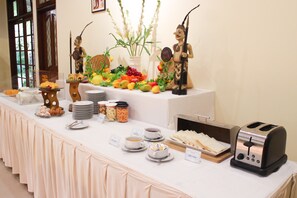 A buffet table with various food items, including fruits, vegetables, and pastries, and a toaster.