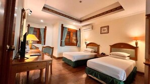 A hotel room with two beds, a desk, a chair, a lamp, and an air conditioning unit. - Kresna (Wonosobo)