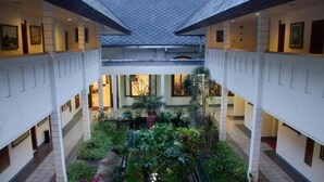 A hotel atrium with a central garden, multiple levels, and framed artwork on the walls. - Kresna (Wonosobo)