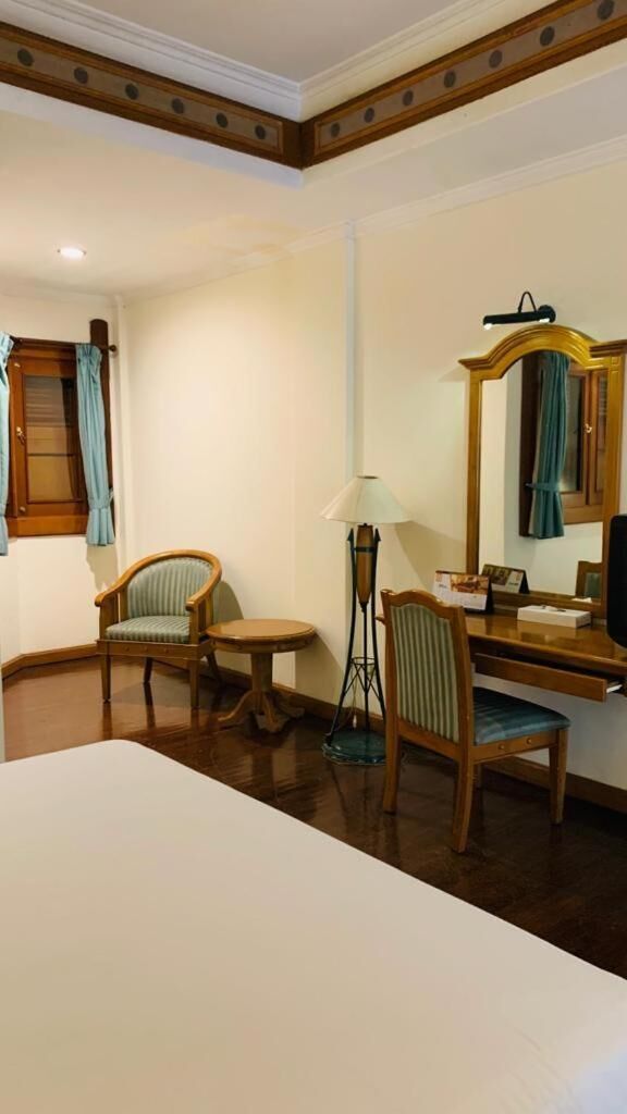 Ein Hotelzimmer mit einem Bett, zwei Stühlen, einem Schreibtisch, einer Lampe, einem Spiegel und einem Fenster mit Vorhängen.