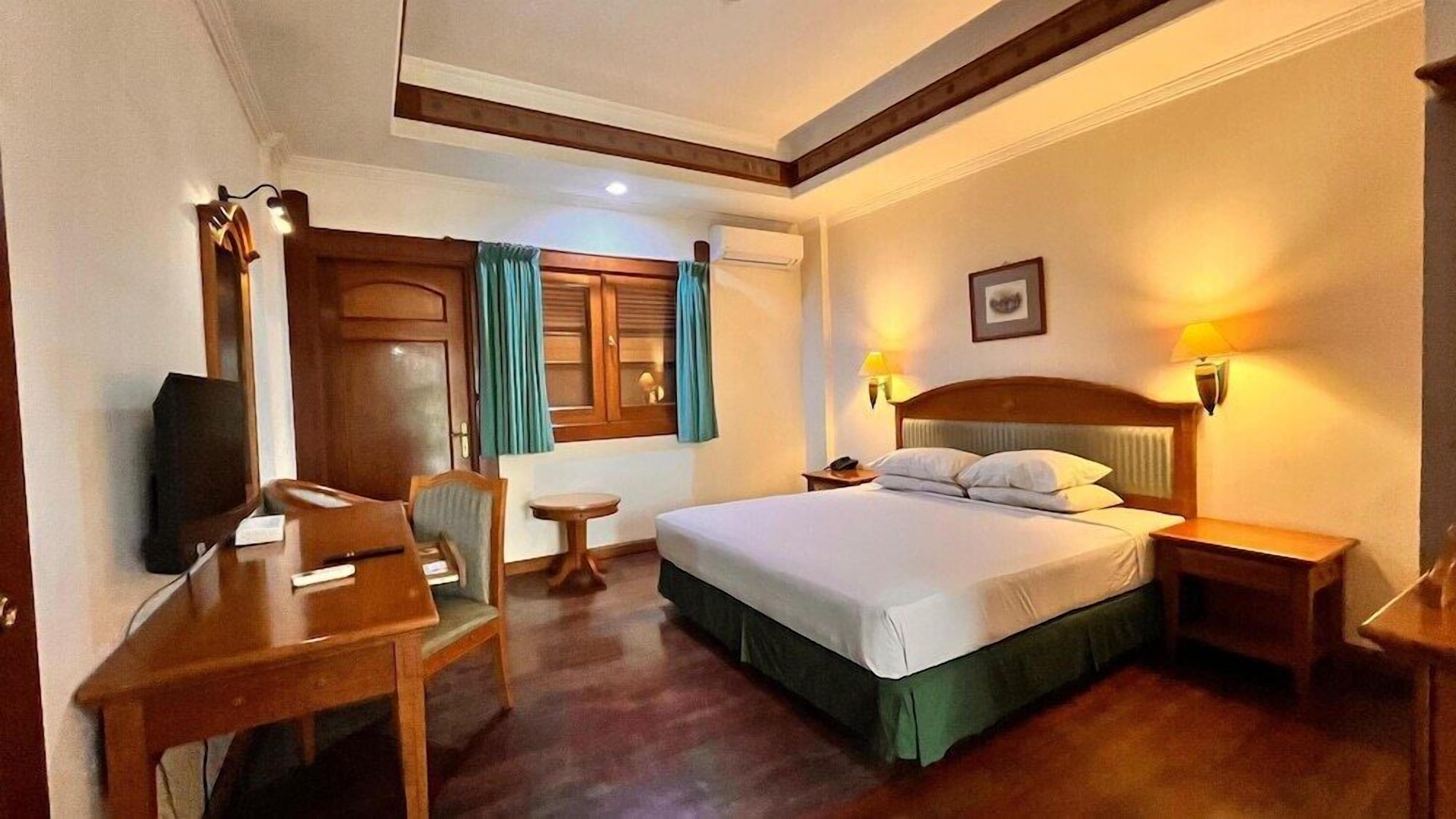 A hotel room with a bed, bedside tables, a desk, a chair, a television, a window with curtains, and a wall-mounted picture.