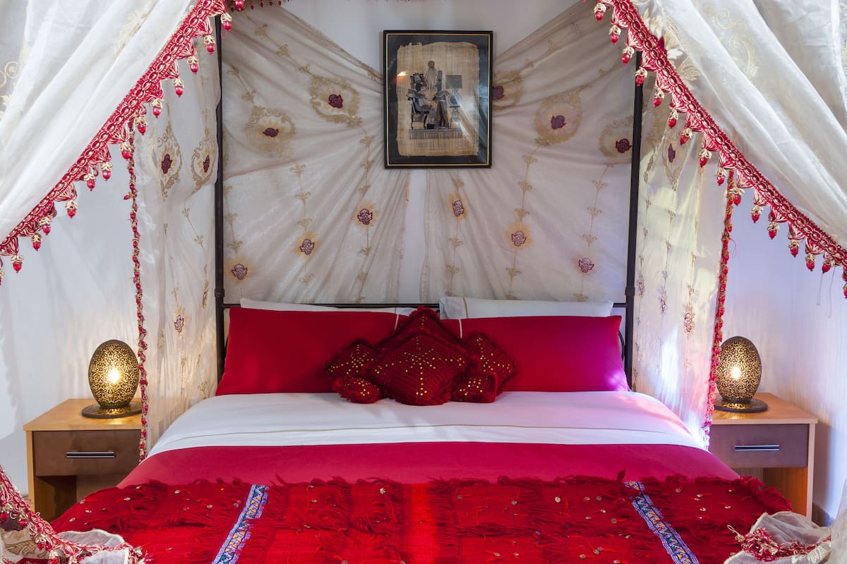 Un lit à baldaquin, des oreillers rouges et un tableau encadré accroché au mur.