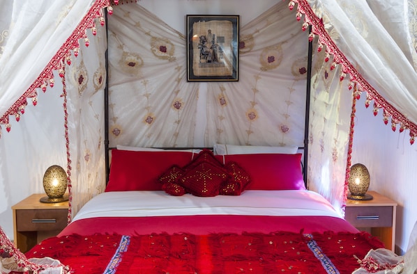 A bed with a canopy, red pillows, and a framed picture on the wall.