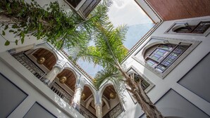 Vista del interior de un edificio con balcones arqueados, un árbol grande y ventanas con diseños.