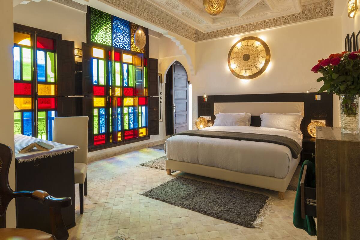Une chambre spacieuse avec un grand lit, un bureau et un vitrail aux couleurs vives.