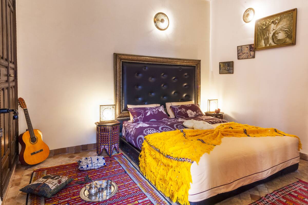 Une chambre à coucher avec un lit, une guitare, une tête de lit décorative et un mur orné de tableaux encadrés.