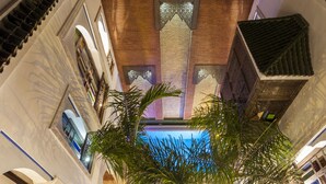 Un atrio espacioso con techos altos, una piscina central, detalles arquitectónicos ornamentales y palmeras.