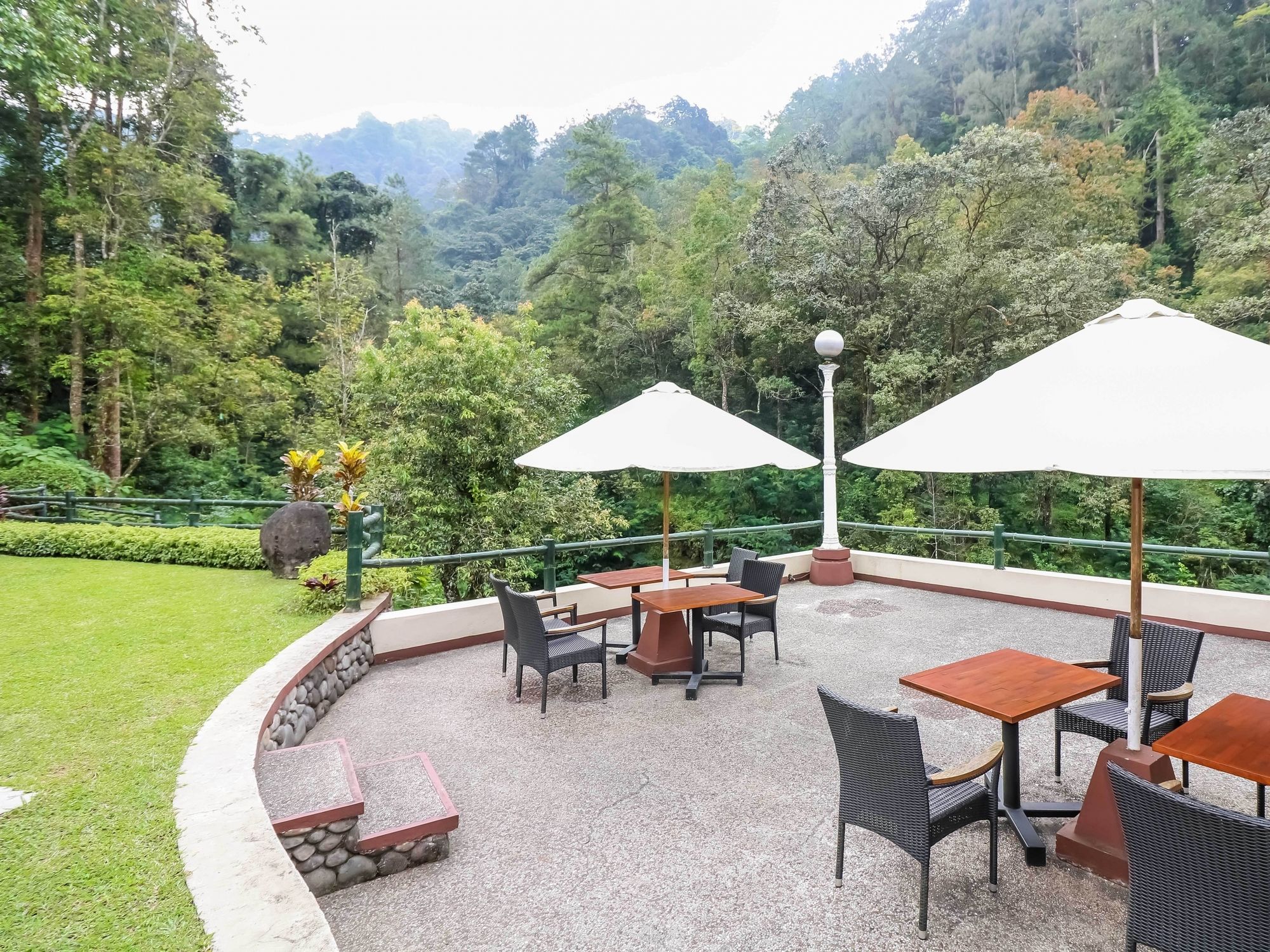 An outdoor patio with tables and chairs, surrounded by a stone wall and greenery.