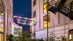 A garden pathway with a variety of plants and flowers, surrounded by buildings with large windows and a decorative metal structure in the background. - Tam Coc Nam Hoa Hotel and Spa (Nam Hoa Lu)