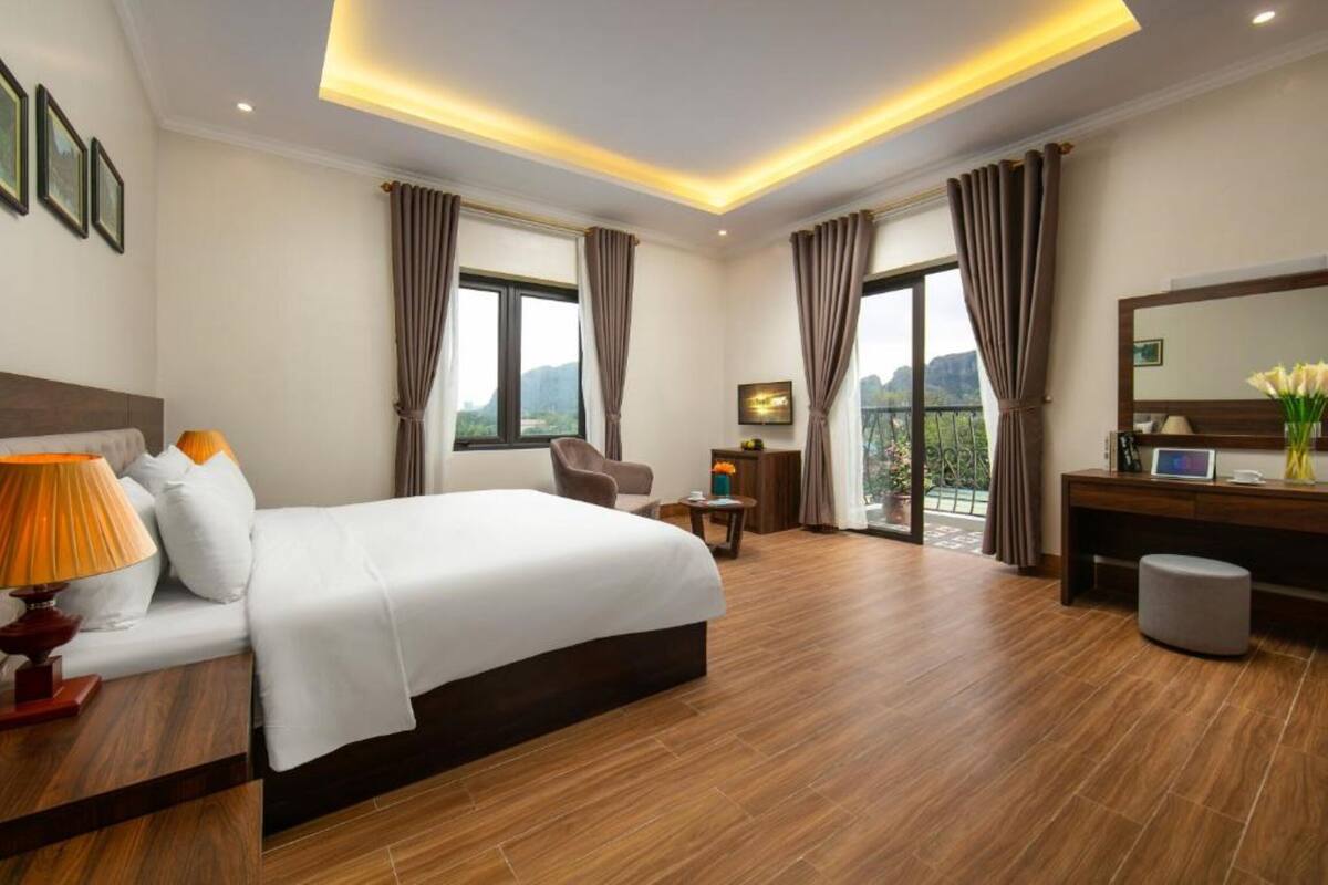 A hotel room with a large bed, a desk, a chair, and a balcony with a view.
