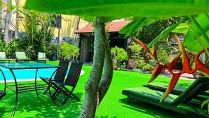 Un área de piscina con sillones de descanso y un edificio pequeño al fondo.