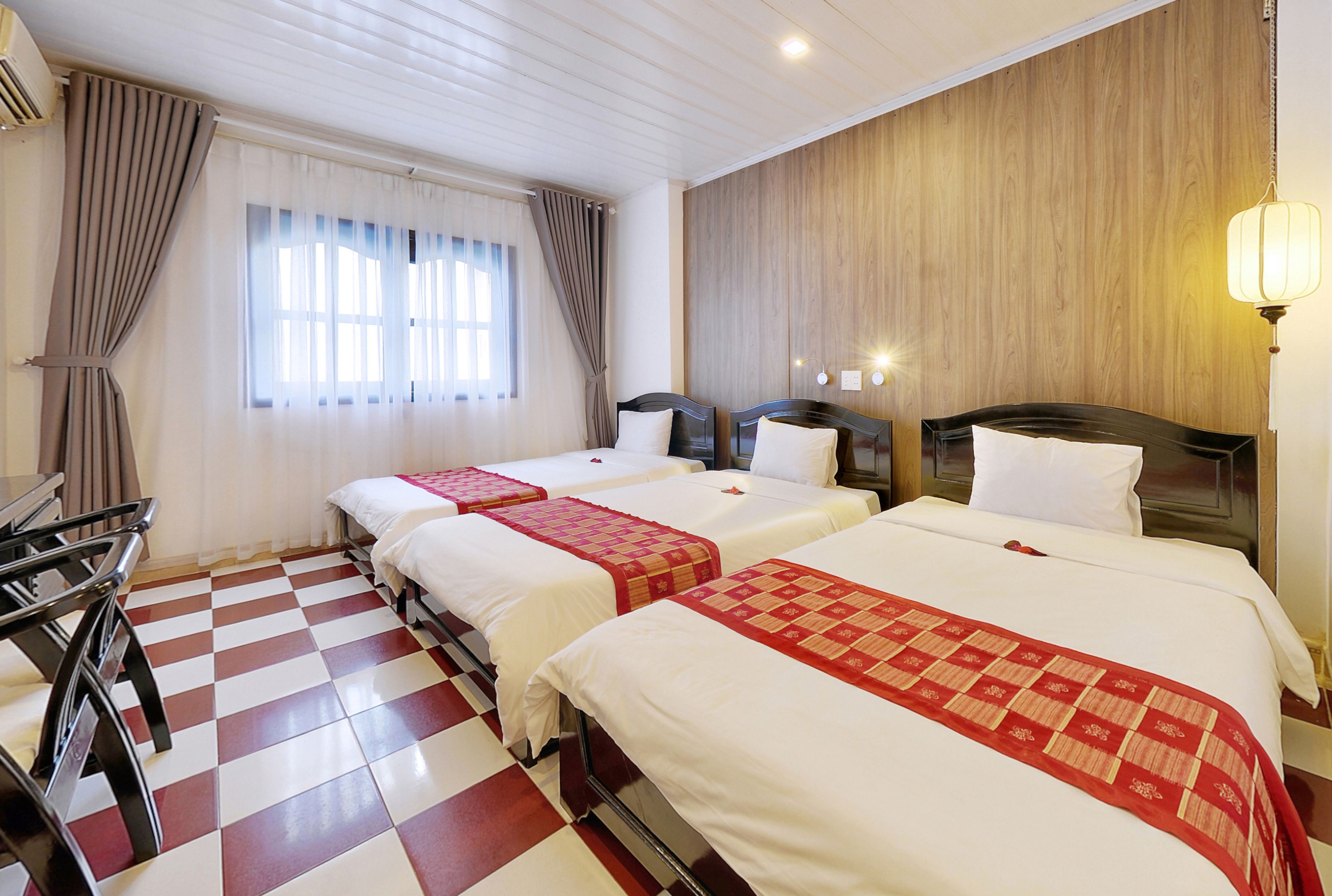 Habitación de hotel con tres camas, piso de cuadros, paneles de madera y una ventana con cortinas.