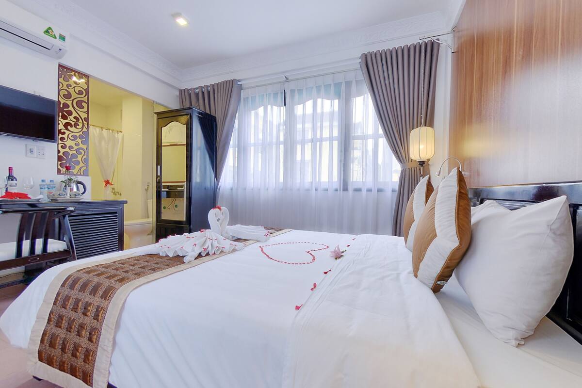 Een hotelkamer met een net opgemaakt bed, een bureau met stoel, een televisie en een spiegel.