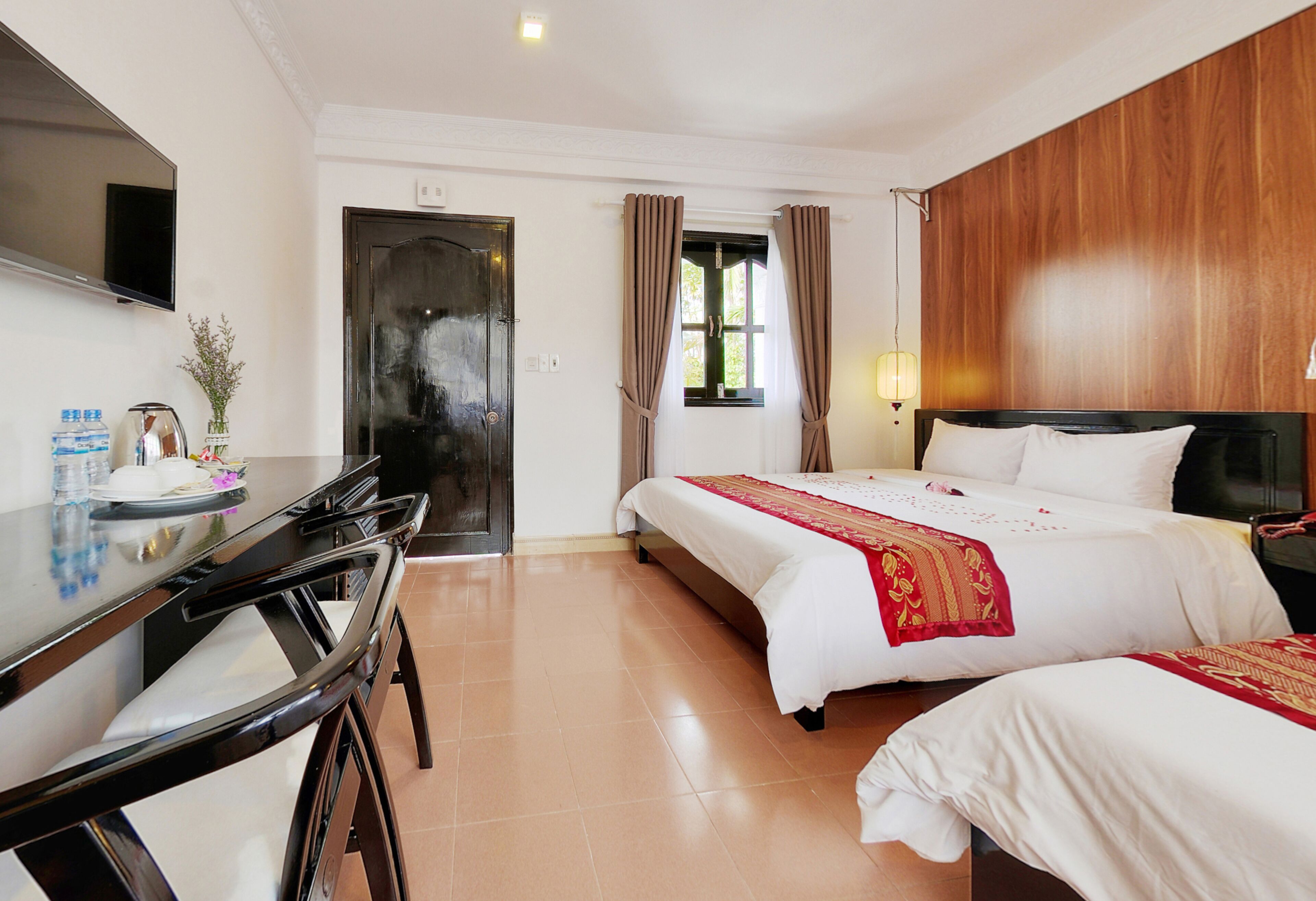 Habitación de hotel con cama, escritorio, televisión y ventana con cortinas.