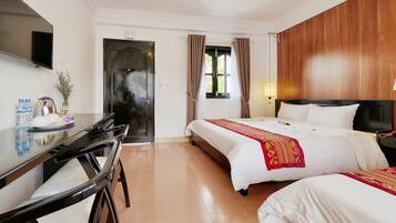 Habitación de hotel con cama, escritorio, televisión y ventana con cortinas.