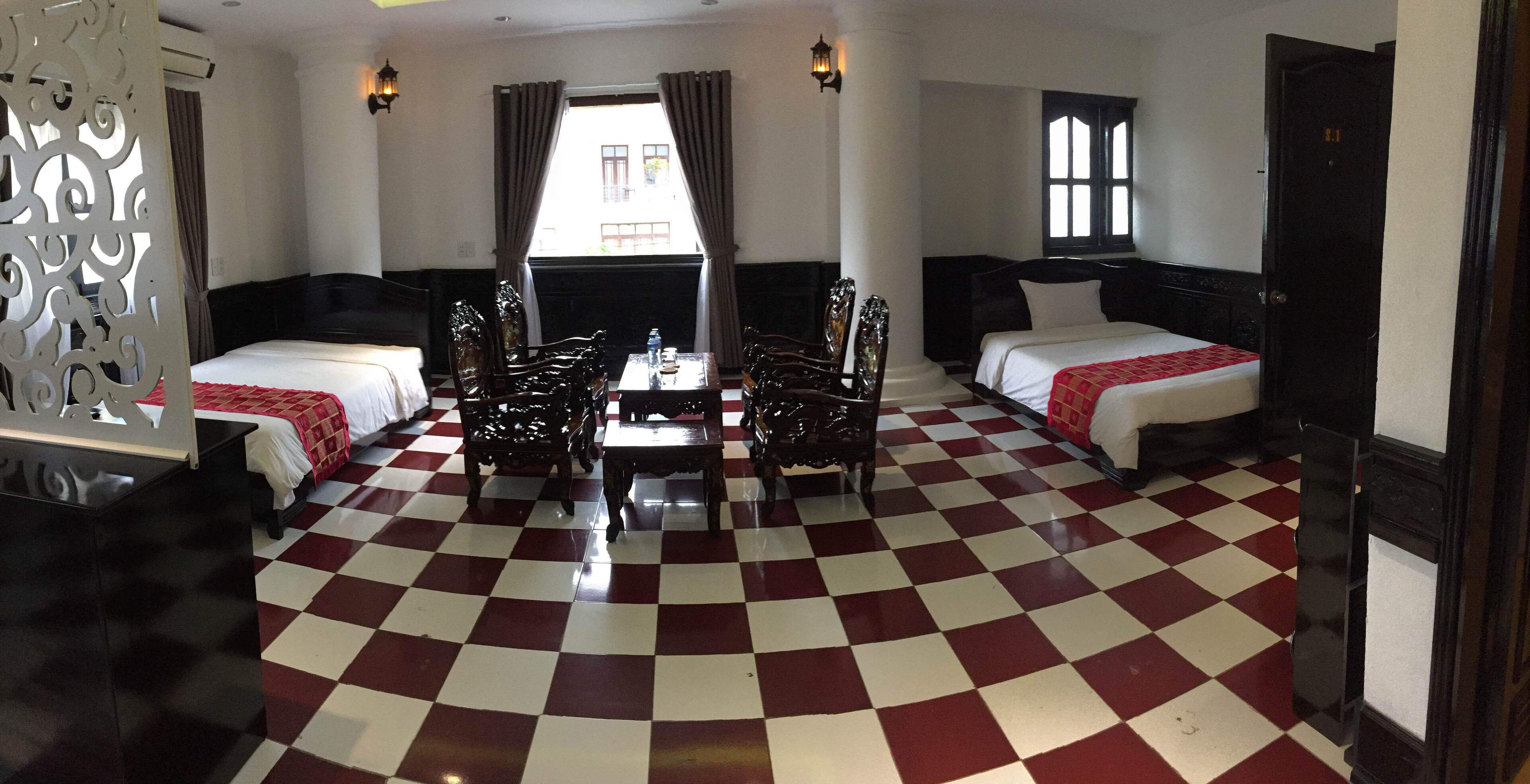 A hotel room with a checkered floor, two beds, a dining table with chairs, and a decorative partition.