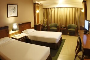 Een hotelkamer met twee bedden, een bureau, een stoel, een lamp, een televisie en een gordijn.
