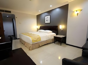 A hotel room with a bed, bedside table, wall-mounted light, and a door leading to another room.