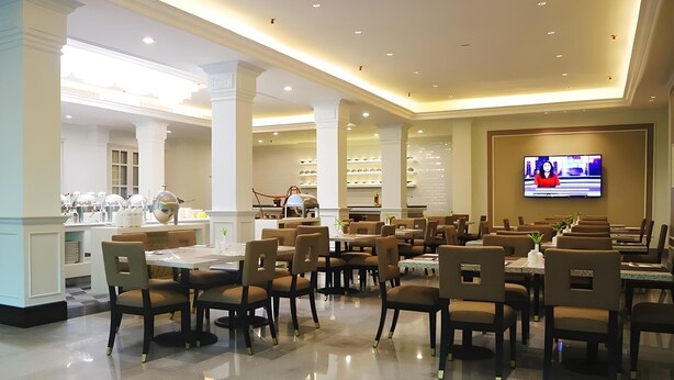 Un grand espace dédié à la salle à manger, avec plusieurs tables et chaises, un écran de télévision et, au fond, un coin cuisine.